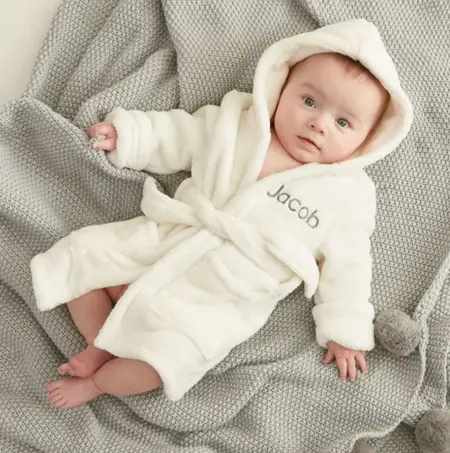 Baby lying on a knitted blanket wearing a personalised hooded bathrobe with the name Jacob